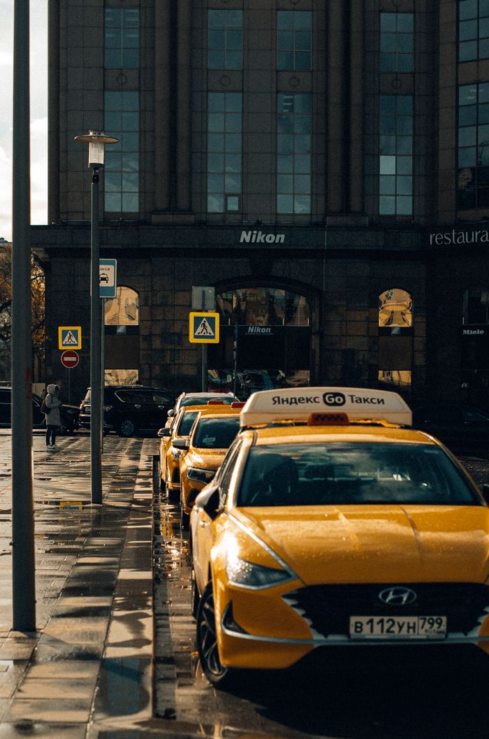 Urban scene featuring parked yellow taxis on a city street in front of a building on a rainy day.